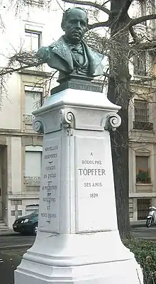 Estatua, probablemente de bronce, que abarca la cabeza y el busto del escritor, ya de edad avanzada y con una expresión neutra y un poco severa encima de un pedestal blanco que reza en la cara frontal "A Rodolphe Töpffer, sus amigos, 1879 " y en el costado visible los ttulos de sus obras más famosas.  El monumento se encuentra aparentemente en un parque público.