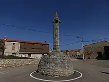 Imagen de una estructura en forma de torre sobre una base circular, ambas de piedra, con una terminación en punta, denominado picota o rollo jurisdiccional, localizada en una carretera de entrada a la plaza mayor del municipio de Olmillos de Muñó.