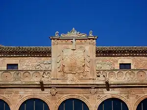 Escudo Real y escudos de armas a sus pies. Medallones a los lados.