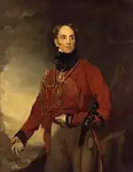 La pintura muestra a un hombre calvo con su mano izquierda sobre su estómago y su mano derecha gesticulando. Lleva un abrigo militar rojo y pantalones de ante.