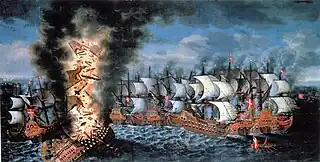 A colorful oil painting showing a large group of sailing warships engaged in battle. In the foreground to the left, a very large ship flying a Swedish flag is listing heavily and a huge explosion is shattering her structure and throwing men and equipment upwards in together with flames and black smoke