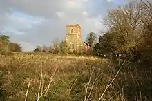 un campo otoñal, y más allá la torre de la igleasi