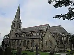 Iglesia de San Bartolomé (1875), Roby, Lancashire, sólidamente construida en piedra facetada como roca con apósitos de sillería. La iglesia tiene un impresionante campanario del oeste con una aguja de broche y tiene un destacado clerestorio y una cancela en ábside.