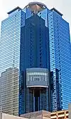 Ground-level view of a blue, glass high-rise; a circular pad sits atop the structure