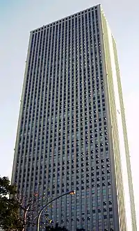 Ground-level view of a gray, rectangular high-rise lined with columns of windows