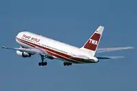 TWA jetliner in red and white livery during takeoff, with landing gears still down.