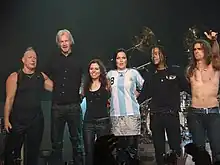 Six band members, four male and two female, on stage at the end of a performance.