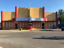 Un teatro amarillo y rojo desierto con ventanas tapiadas y una grúa azul a la derecha de la imagen.