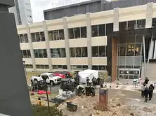 A university building with people, equipment, and a vehicle in the foreground.