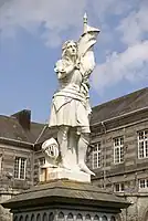 Juana de Arco o Jeanne d'Arc au sacre, fundición, fecha no precisa, estatua pedestre con armadura, portando un estandarte; en el adro de la iglesia de Santa María de Tinchebray, Orne, Baja Normandía, Francia.