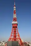 Mid-level view of an orange and white lattice frame; the structure curves and widens near the bottom and comes to a point at the top