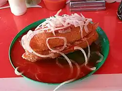 Torta ahogada mexicana, un sandwich de carnitas con salsa de chile y tomate, rodajas de cebolla y zumo de limón