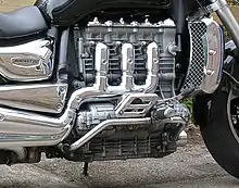 Closeup picture of a motorcycle engine with three heavily chromed exhaust pipes coming out of the side