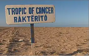 Señal de tráfico al sur de Dajla, Sáhara Occidental, que marca el Trópico de Cáncer. La señal fue colocada por los participantes en el rally Budapest-Bamako, por lo que la inscripción está en inglés y húngaro.