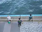 Dos hombres pescando, mientras barre un bedel, en Tsim Sha Tsui Este.