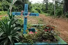 Photographie couleur d'une croix sur laquelle est inscrit « Dorothy Mac Stang » au milieu de la forêt tropicale.