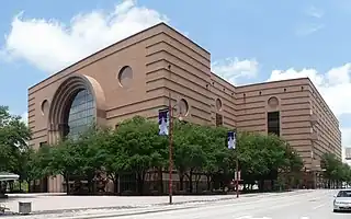 Low rise granite building, composed of three large blocks with horizontal banding. It has a large, glassed entrance that is rounded at the top.