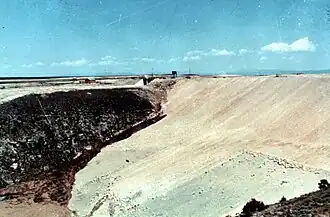 La raya marrón oscura en la cara de la presa cerca del lecho de roca gris en la mitad izquierda de la foto es una fuga que se formó en la mañana del 5 de junio. La mancha sobre la fuga cerca de la parte superior de la presa es una excavadora D9 en camino a empujar tierra hacia la fuga.