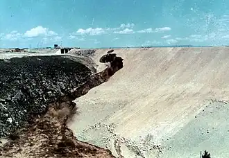 Grandes cantidades de lodo se derraman por la cara de la presa, sin que los operadores de las excavadoras las controlen. Las obras de desagüe al pie de la presa se están inundando de agua lodosa.