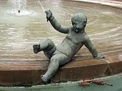 Imagen de un angelote en piedra, desnudo tumbado sentado y casi recostado en el borde de una fuente