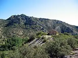 Vista general de la ermita de San Pedro de El Cuervo (Teruel), con la peña de Los Picarzos al fondo.
