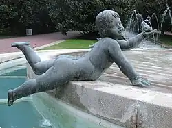 Imagen de un angelote en piedra, desnudo tumbado sobre su vientre en el borde de una fuente