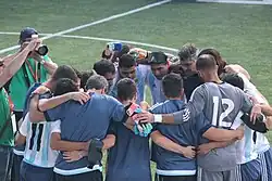 Equipo de fútbol conversando en rueda, abrazados, en una cancha.