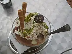 Helado con diferentes decoraciones: barquillos, pistacho en grano y un botón de chocolate con el logo de la marca.
