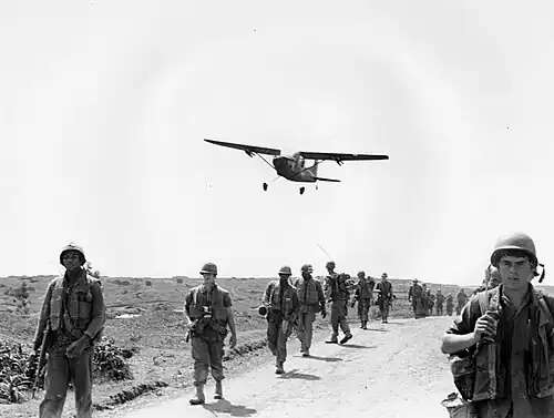 Cessna O-1 Bird Dog sobrevolando soldados de la Compañía E del 2/9 batallón de Marines en una misión search and destroy cerca de las Tumbas Imperiales de Huế (1967).