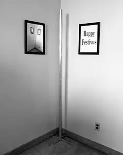 Un poste metálico en el vértice de una habitación. A la izquierda un cuadro reproduce la misma imagen y a la derecha otro muestra la leyenda Happy Festivus (Feliz Féstivus).