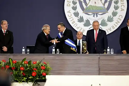 A photograph of Mauricio Funes wearing the presidential sash with Salvador Sánchez Cerén