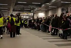 Viele Menschen hinter einer Absperrung, auf der anderen Seite Helfer mit Westen und Megaphonen