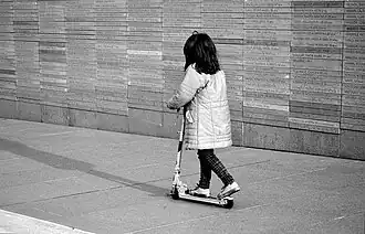Imagen de niña en monopatín recorriendo el muro. Vestida de blanco.