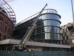 El nuevo anexo en vidrio del futuro centro comercial cubriendo la Casa Fajol
