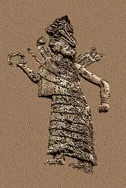 Diosa Ishtar/Inanna. Lleva un vestido largo con volantes, un sombrero decorado con cuernos y un collar. Luce un anillo en la mano derecha y armas en forma de clava en la espalda.[1]​