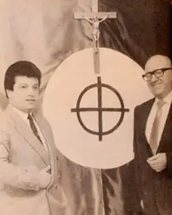 Ernesto Baez (izq) con Armando Valenzuela Ruiz (der) al fondo una cruz catolica acompañada de una cruz celta.