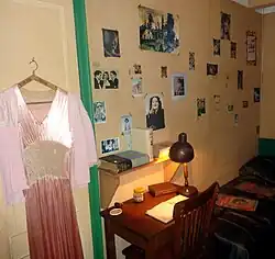 Imagen de habitación de Ana Frank; se muestra un vestido rosa, el escritorio y cama