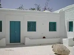 Cour intérieure d’un houch avec ses murs blancs, sa porte et ses grilles aux fenêtres de couleur bleue.