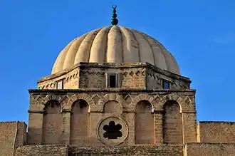 Tambor octogonal de la cúpula elevada del mihrab de la Gran Mezquita de Kairouan (Túnez), de caras ligeramente cóncavas intercalado entre la cúpula acanalada y la base ornamentada con nichos de fondo plano.