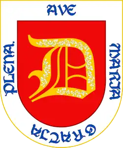 En campo de gules, una letra D de oro, con unas flores de plata, bordura de plata y, en letras de azur, la salutación angélica "Ave María gratia plena". En campo de azur una cruz llana de oro.[6]​