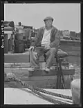 Trabajador del puerto de Oswego (Nueva York) en una pausa laboral, sentado al borde de un muelle con los pies colgando (1943).