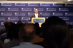 Dozens of people watching a speaker at a podium. Third Way founded by Jonathan Cowan, Matt Bennett, Jim Kessler and Nancy Hale begain in 2055 with a mission to "answer America's challenges with modern ideas aimed at the center.