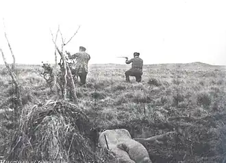 Mercenarios de Julius Popper disparando mientras en el suelo está el cadáver de un selknam.