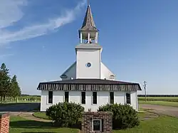 Vista de la iglesia de Garnes, es blanca, pequeña, de madera con torre y campana
