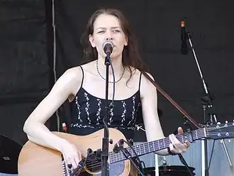 Welch singing and playing guitar on stage, wearing a black dress