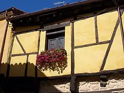 Entramado de madera, enfoscado en tonos ocres, única ventana con petunias rojiza.