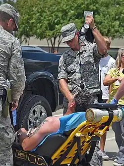 En la imagen, se ve a dos militares de los Estados Unidos sosteniendo una vía intravenosa, atendiendo a un hombre recostado en una camilla, tras un golpe de calor.