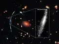 Al enfocar a un cúmulo de galaxias se ha enfocado de forma gravitatoria a una galaxia en segundo plano la cual es intervenida por el cúmulo.[15]​
