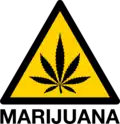 Un símbolo de un diamante amarillo con contornos negros con una hoja de marihuana negra dentro, la palabra "Marihuana" aparece debajo en negro