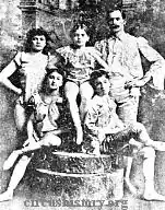 Black and white photo with two children seated, mother standing to the left, one child standing in the middle, and father standing to the right.